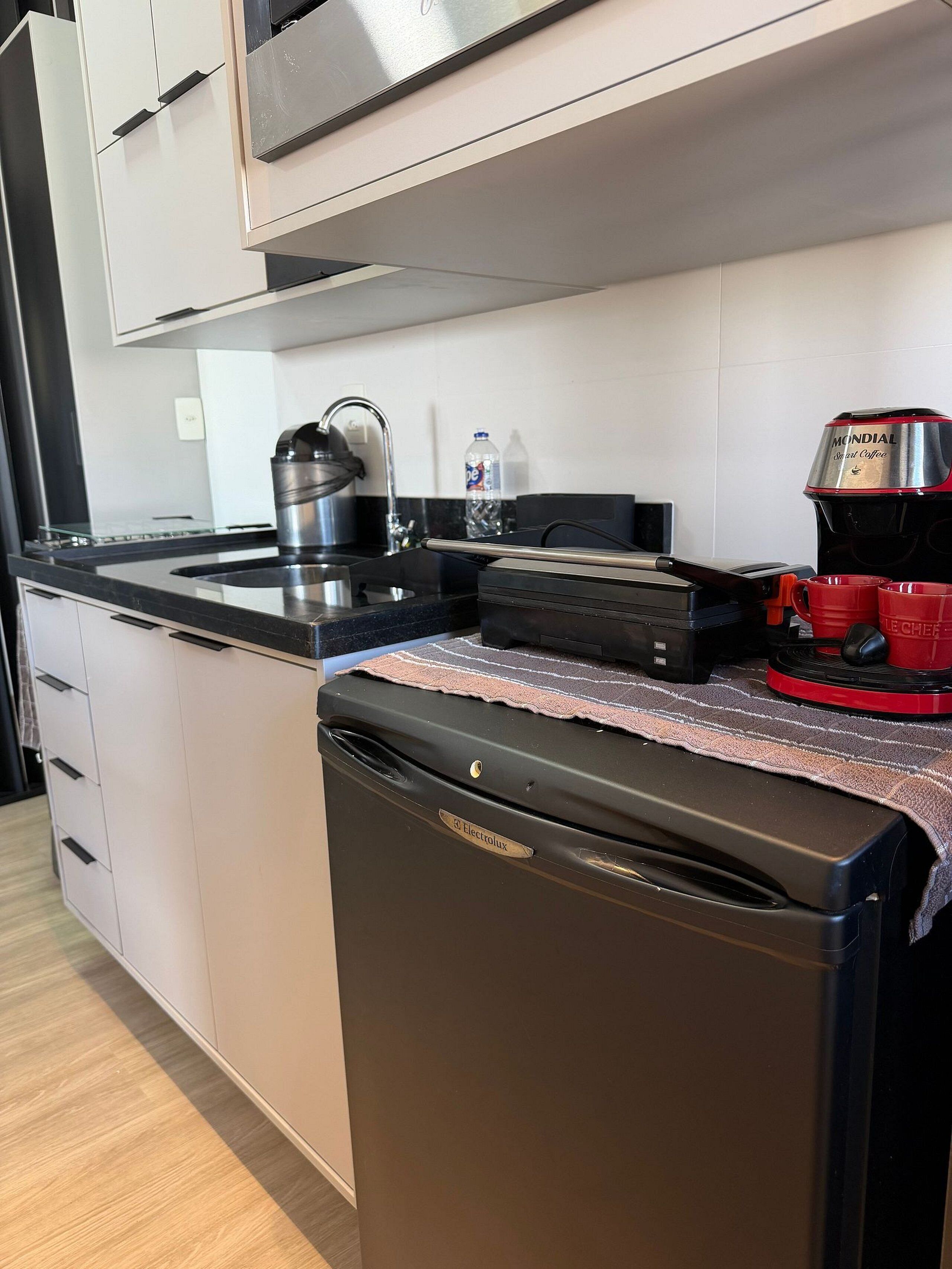 A compact kitchen with a dishwasher, a coffee maker, and a kettle.