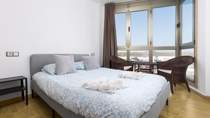 Hotelkamer met een groot bed, uitzicht op de woestijn door een raam, een rieten stoel en een klein tafeltje.