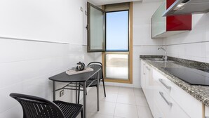 Een kleine keuken met witte kastjes, een granieten aanrecht, een eettafel met stoelen en een raam met uitzicht.