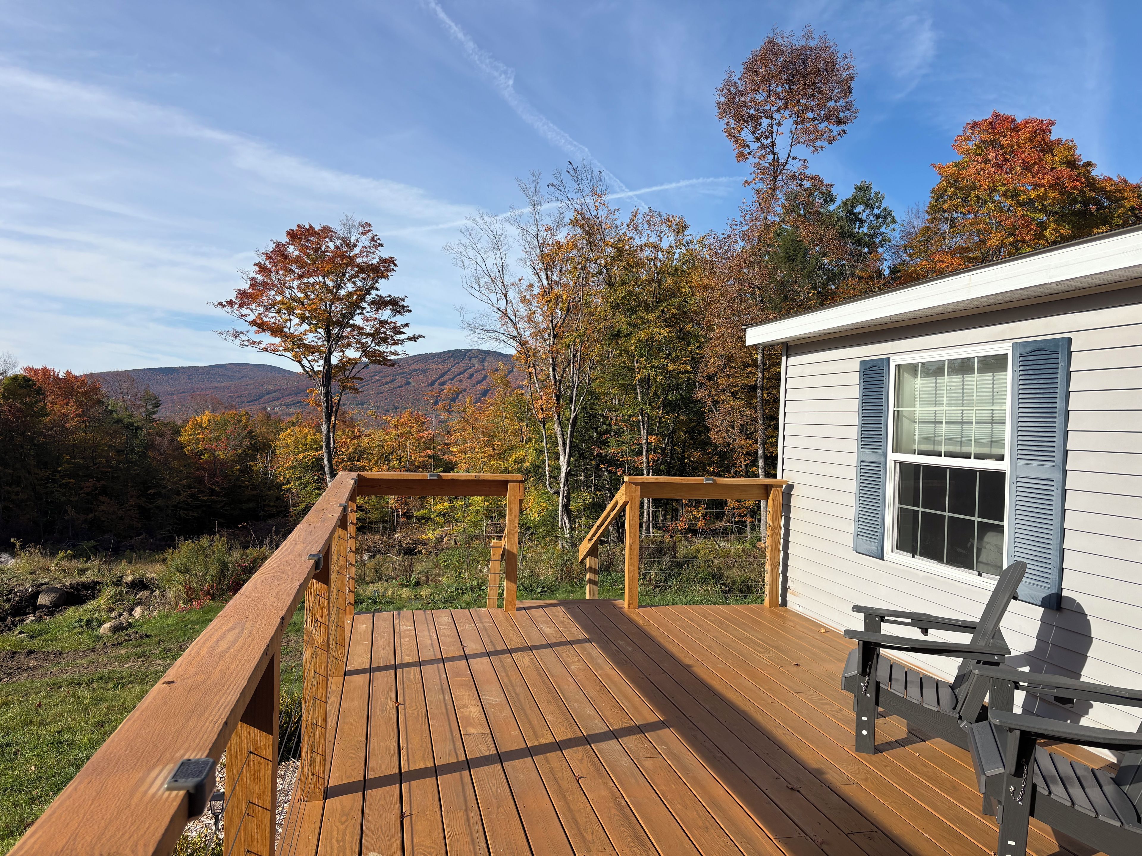 Una terraza de madera con vistas a una cadena montañosa y follaje otoñal.