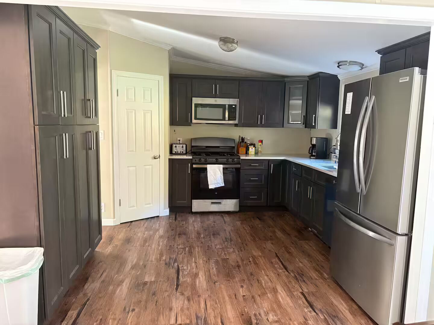 A kitchen with dark cabinets, a stainless steel refrigerator, a microwave, a stove, and a toaster.