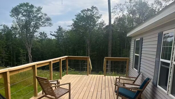 Ett trädäck med två gungstolar och en solstol, omgivet av ett trästaket och med utsikt över ett skogsområde.