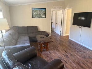 A living room with a sectional sofa, a coffee table, and a flat-screen TV mounted on the wall. - Fabulous 4-bedroom house in Ludlow perfect for your ski getaway (Ludlow)