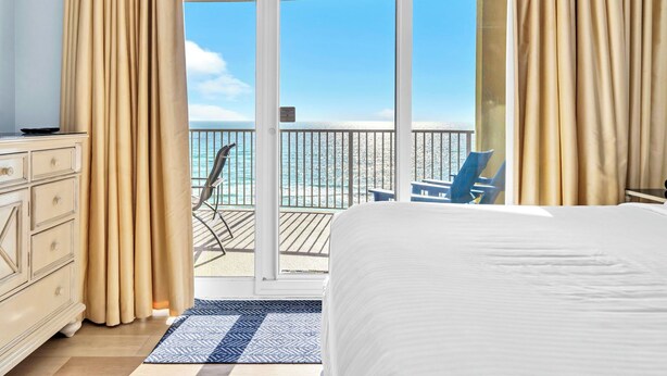 Ett hotellrum med en stor säng, en byrå och utsikt över havet genom en skjutdörr av glas.
