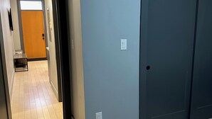 A hallway with a wooden floor, a door with a light switch, and a small table with a trash bin. - Cozy 1-bedroom apartment in brilliant Cincinnati with AC (Cincinnati)