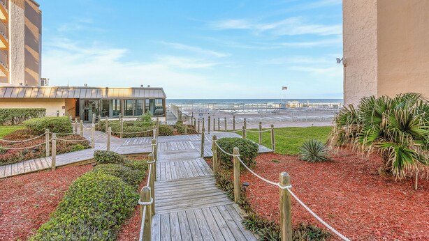 A wooden pathway leading to a building with a view of the beach. - 🏖️Oceanfront | 1st Floor | Steps to Pool and Beach | Castle Reef 113🏖️ (New Smyrna Beach)