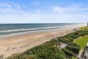 Blick auf einen Strand mit einer Holzterrasse und einer Rasenfläche.