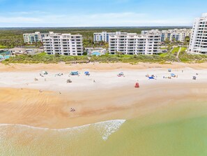 Ein Strand mit mehreren Gebäuden im Hintergrund, einige davon mit Balkonen.
