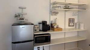 A kitchenette with a refrigerator, microwave, toaster, and shelves with kitchenware.