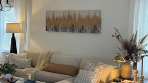 A living room with a sectional sofa, a coffee table, a lamp, a vase with flowers, and a painting on the wall.