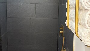 A shower with dark tiles, a gold towel rack, and a showerhead.