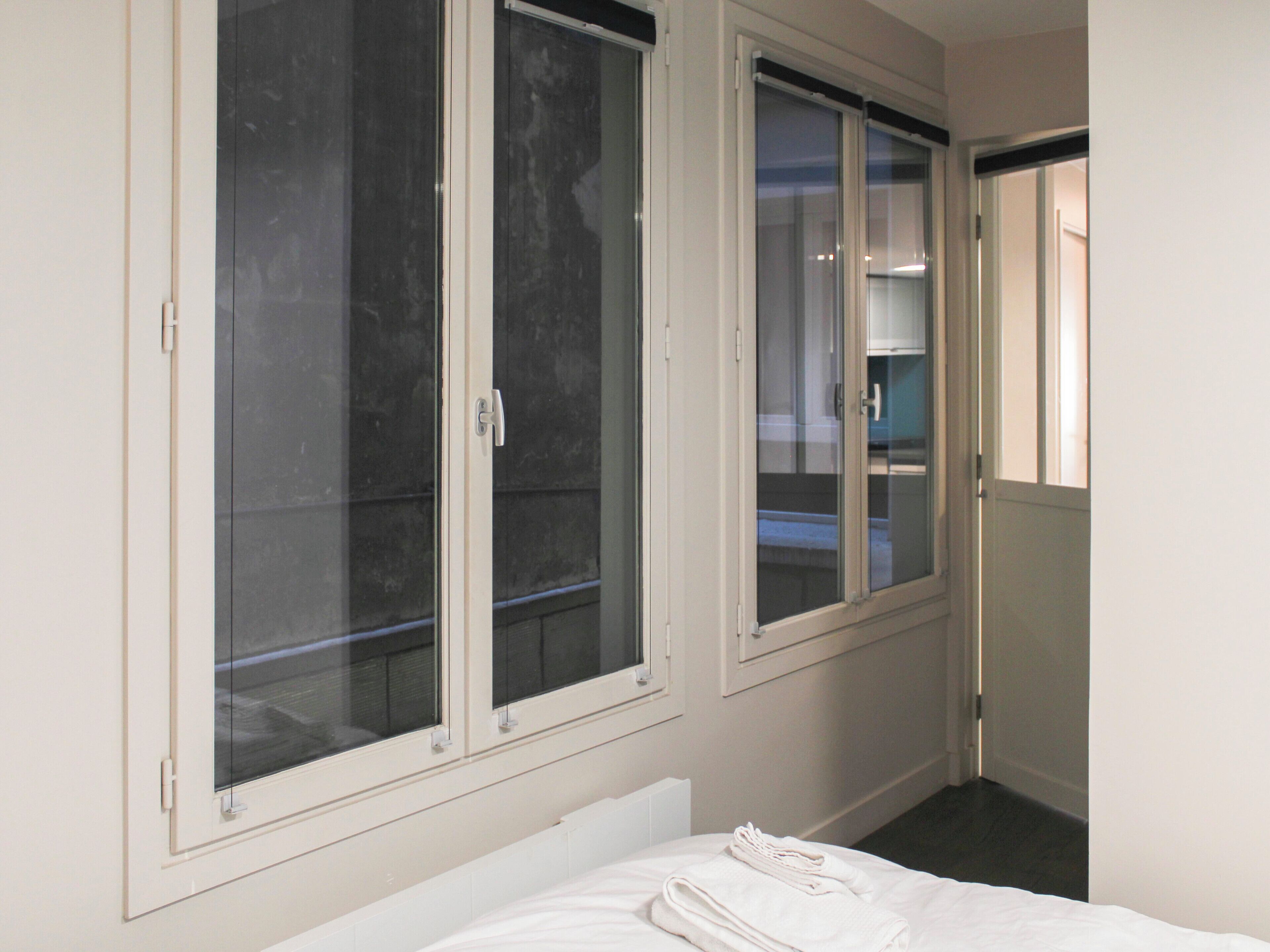 Una camera d'albergo con un letto, una finestra vista e una porta che dà su un corridoio.