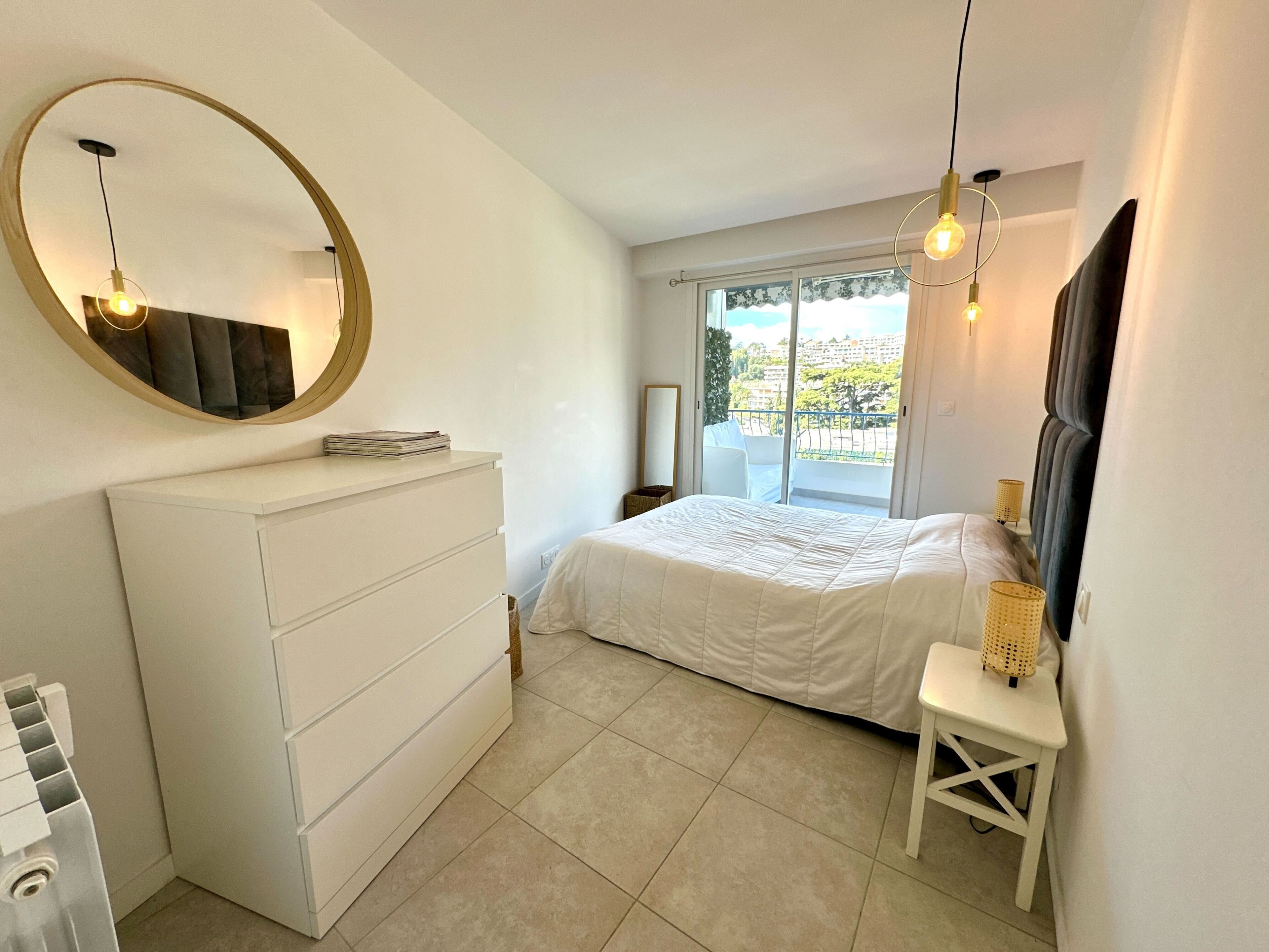 Une chambre à coucher avec un lit, une commode, un miroir et un balcon offrant une vue.
