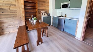 Una cocina compacta con estantes de madera, una mesa de comedor con sillas y un microondas.