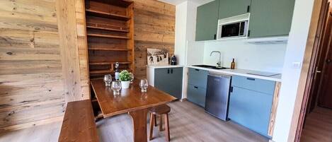 A compact kitchen with wooden shelves, a dining table with chairs, and a microwave.