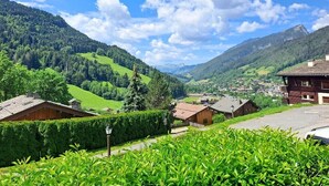 Un pueblo rural con casas de madera tradicionales, cielo despejado y colinas verdes exuberantes al fondo.