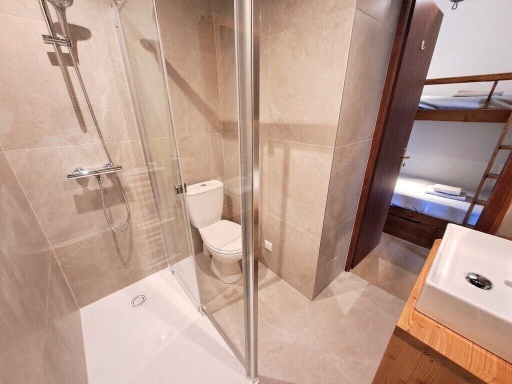 Casa de banho com cabine de duche de vidro, sanita e lavatório.