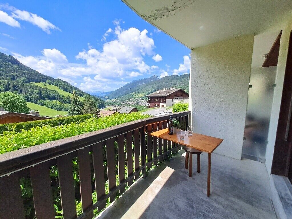 A balcony with a table and chairs, overlooking a green valley and mountains.