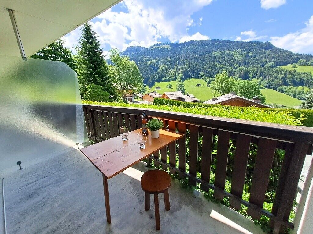 Un balcon avec une table et des chaises en bois, donnant sur un paysage montagneux parsemé de maisons.