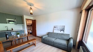 Una sala de estar con un sofá gris, una mesa de comedor de madera y una cocina al fondo.