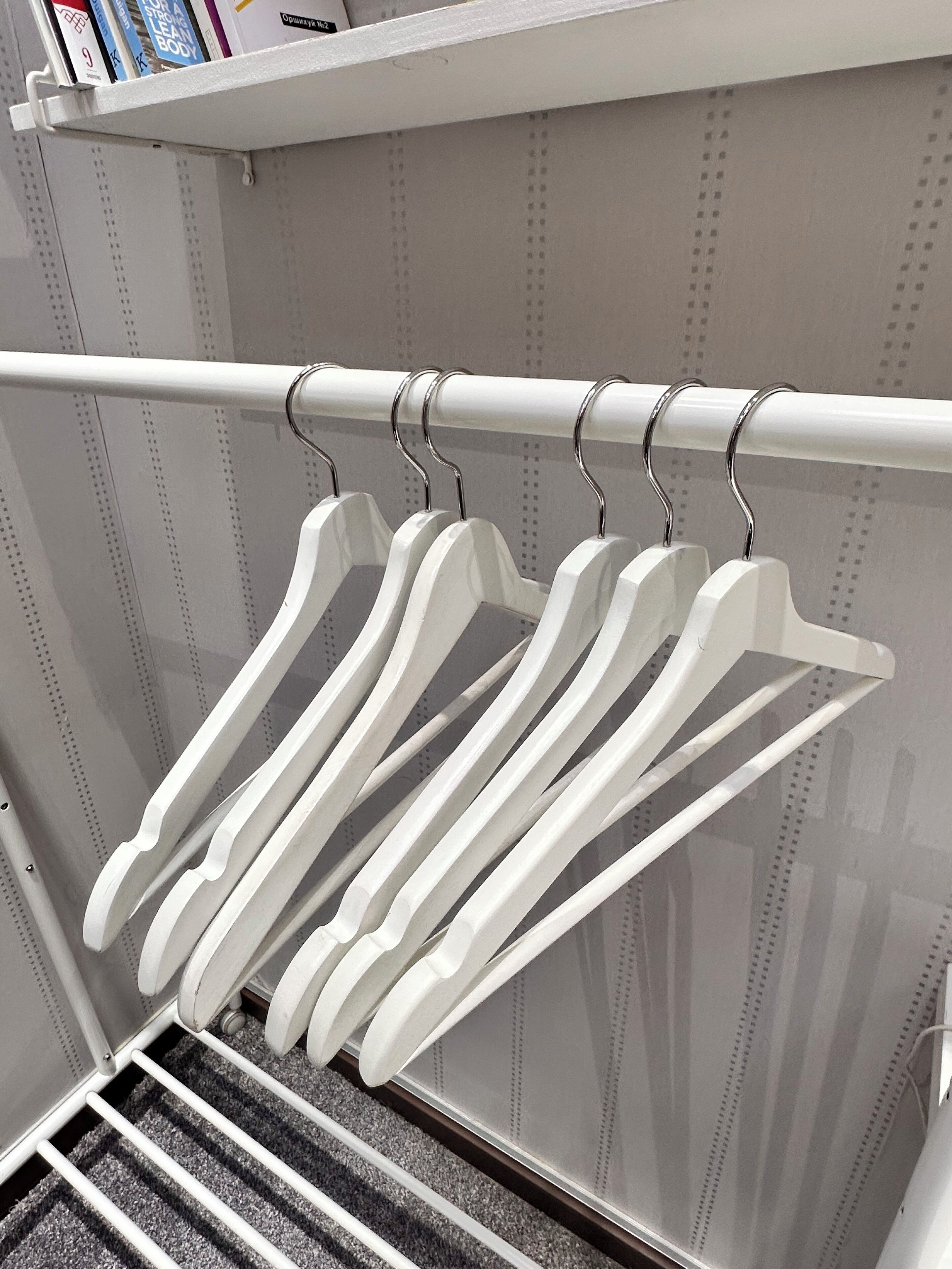 A white metal rack with multiple white hangers against a wall with a perforated pattern.