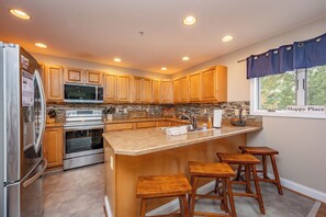 A modern kitchen with wooden cabinets, stainless steel appliances, a granite countertop, and a bar area with stools. - New! Lake Access Home in Deep Creek w/ Hot Tub (Oakland)