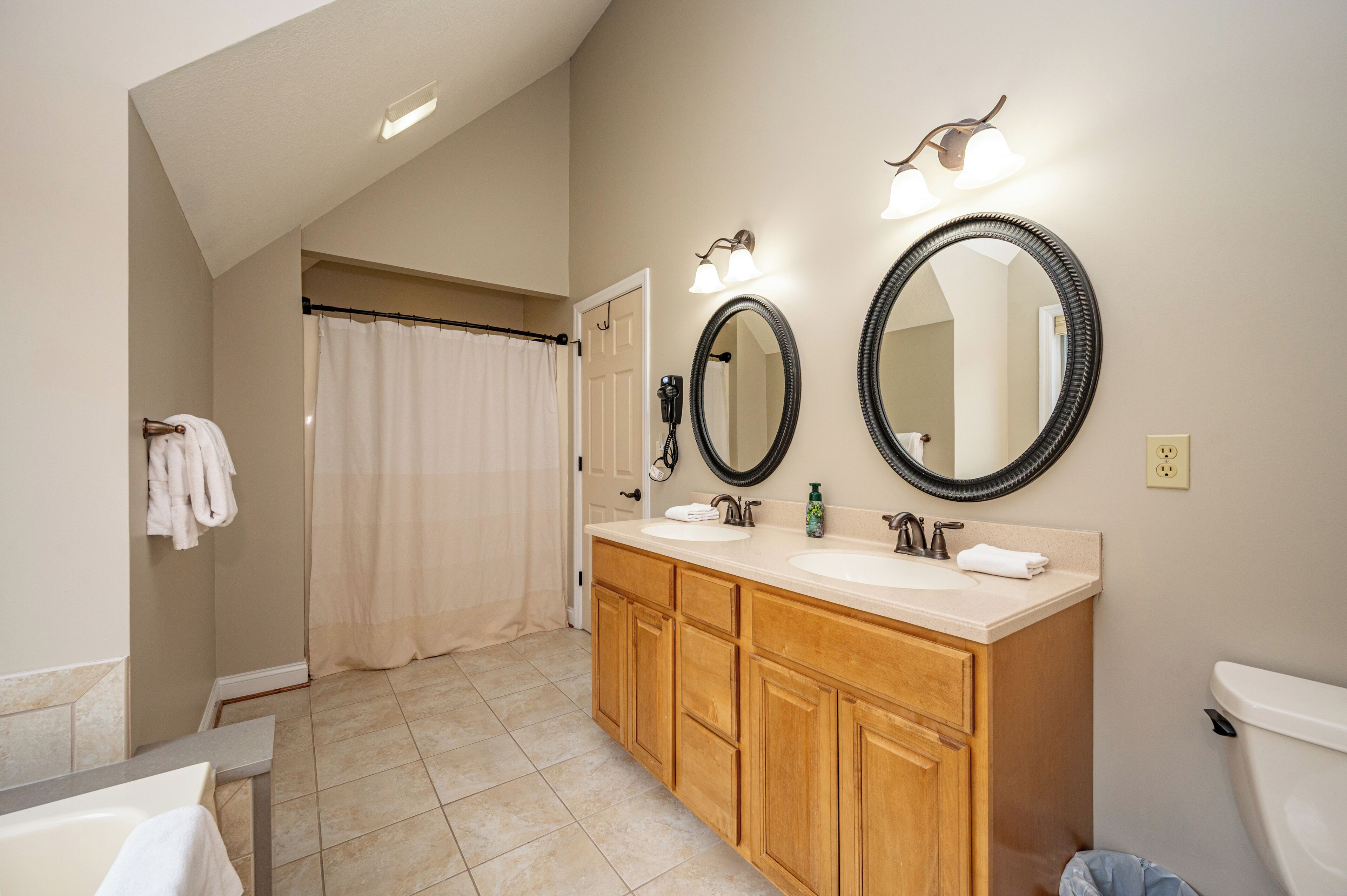 A bathroom with a double vanity, two mirrors, a shower curtain, and a toilet.