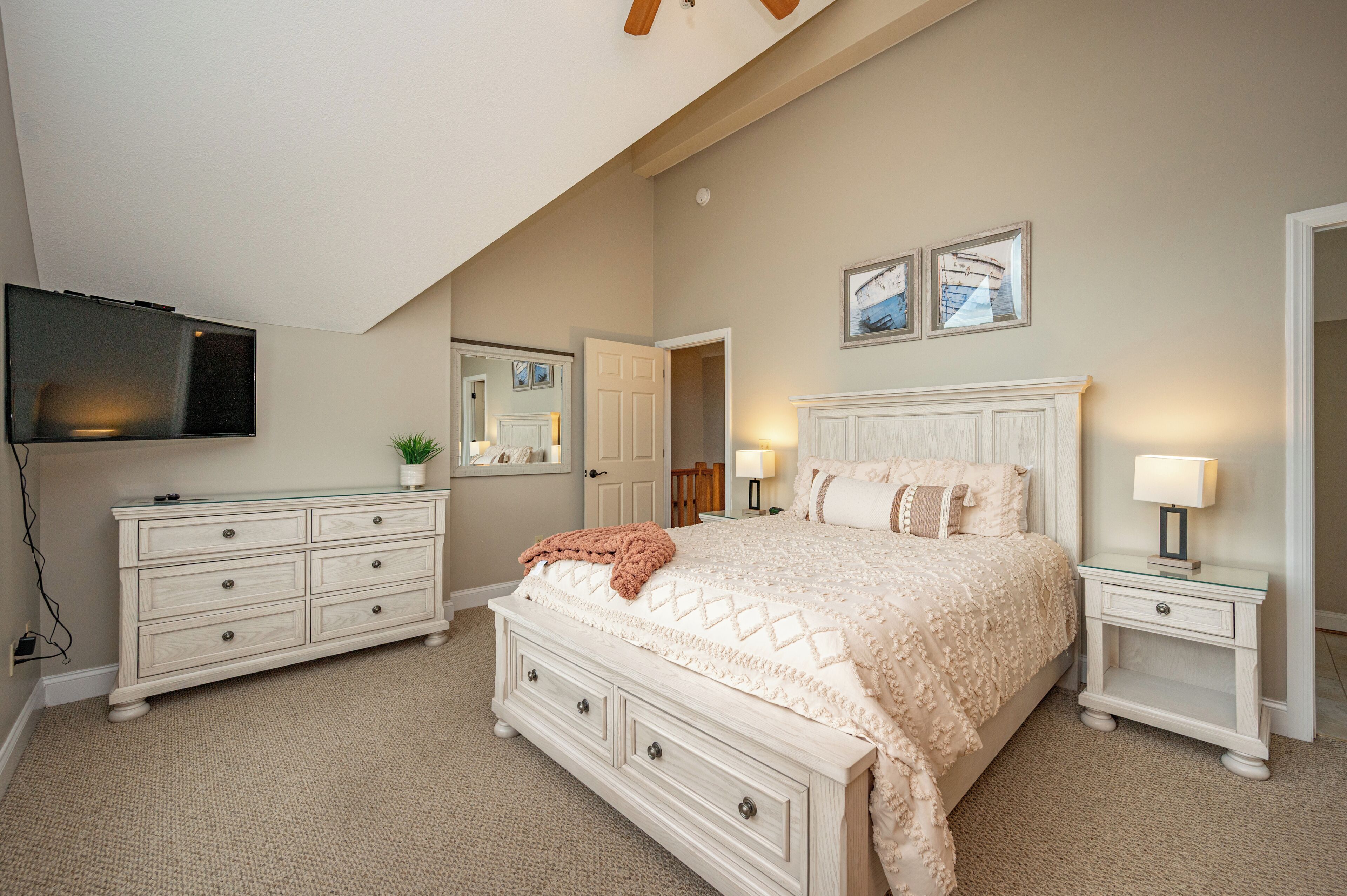 A bedroom with a bed, dresser, nightstands, a television, and a mirror.