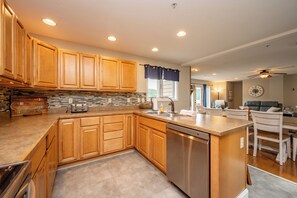 A modern kitchen with wooden cabinets, a built-in dishwasher, and a stone backsplash. - New! Lake Access Home in Deep Creek w/ Hot Tub (Oakland)