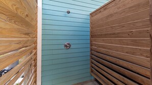 Una terraza de madera con un muro exterior azul, una puerta de metal y un picaporte de metal.
