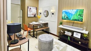 A modern living room with a flat-screen TV, a dining area, and a seating area with a round ottoman. - Condo in Davao City - 2BR Penthouse @ Verdon Parc (Davao City)