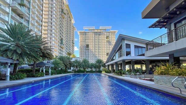 A swimming pool with a clear blue water surface, surrounded by tall residential buildings and palm trees. - Condo in Davao City - 2BR Penthouse @ Verdon Parc (Davao City)