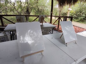 An outdoor seating area with white tables and chairs, surrounded by trees and a wooden fence.
