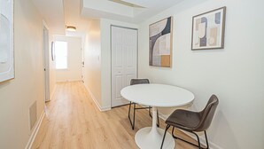 Un pasillo con una puerta blanca, una mesa redonda con dos sillas y obras de arte en la pared.