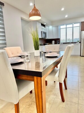 Een moderne eetruimte met een houten tafel, witte fauteuils en een hanglamp.