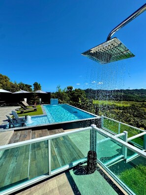 Ein moderner Außenpool mit einer verglasten Poolterrasse, Liegestühlen und einer Dusche.