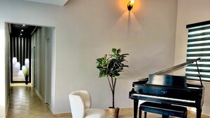 Ein geräumiges Zimmer mit einem Klavier, einem weißen Sessel und einer Topfpflanze.