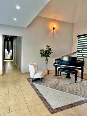 Een ruime kamer met een piano, een witte fauteuil en een plant in pot.