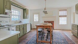 Eine Küche mit grünen Schränken, einem Holztisch, Barhocker und einem gemusterten Teppich.