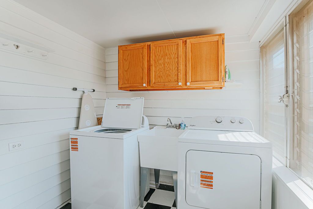 Une buanderie équipée de deux machines à laver, d’un sèche-linge et de placards en bois situés au-dessus.