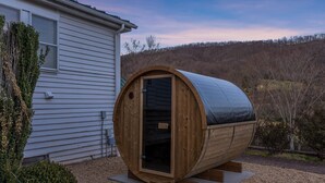 Eine Holzzelt-Sauna mit Tür, auf Kiesboden in der Nähe eines Hauses platziert.