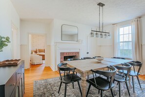 A dining area with a wooden table and black chairs, a fireplace, and a large window with curtains. - Barrel Sauna, Hot Tub & Views (Roseland)
