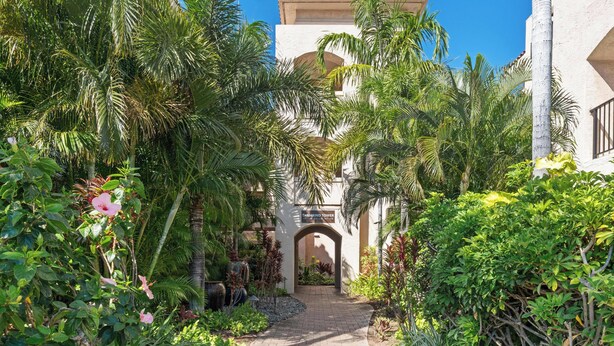 A pathway leading to a building with an arched entrance, surrounded by lush greenery and palm trees. - Perfect for a couples getaway!  311 Shores at Waikoloa (Waikoloa Beach Resort)