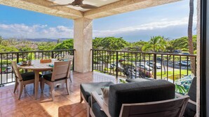 A balcony with a table and chairs, a ceiling fan, and a view of a parking area and greenery. - Perfect for a couples getaway!  311 Shores at Waikoloa (Waikoloa Beach Resort)
