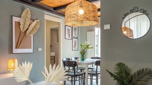 Een moderne eethoek met een glazen tafel, zwarte stoelen en een pendelarmatuur van riet.