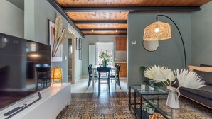 Een moderne woonkamer met een flatscreen-tv, een eethoek met een tafel en stoelen, een bank en een decoratieve lamp.