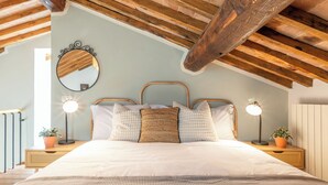 Een slaapkamer met een houten plafond, een bed met witte beddengoed, twee nachtkastjes met lampen en een spiegel aan de muur.