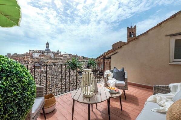 A rooftop terrace with a view of historic buildings, a table with a vase and a plate of food, and a comfortable seating area. - Apartment Paradise-in the center with a terrace with a view (Siena)