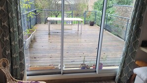 Un terrazzo in legno con tavolo e sedie, circondato da piante in vaso e da una ringhiera.