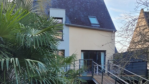 Una casa moderna con tetto spiovente, un patio in legno e un piccolo giardino con palme.